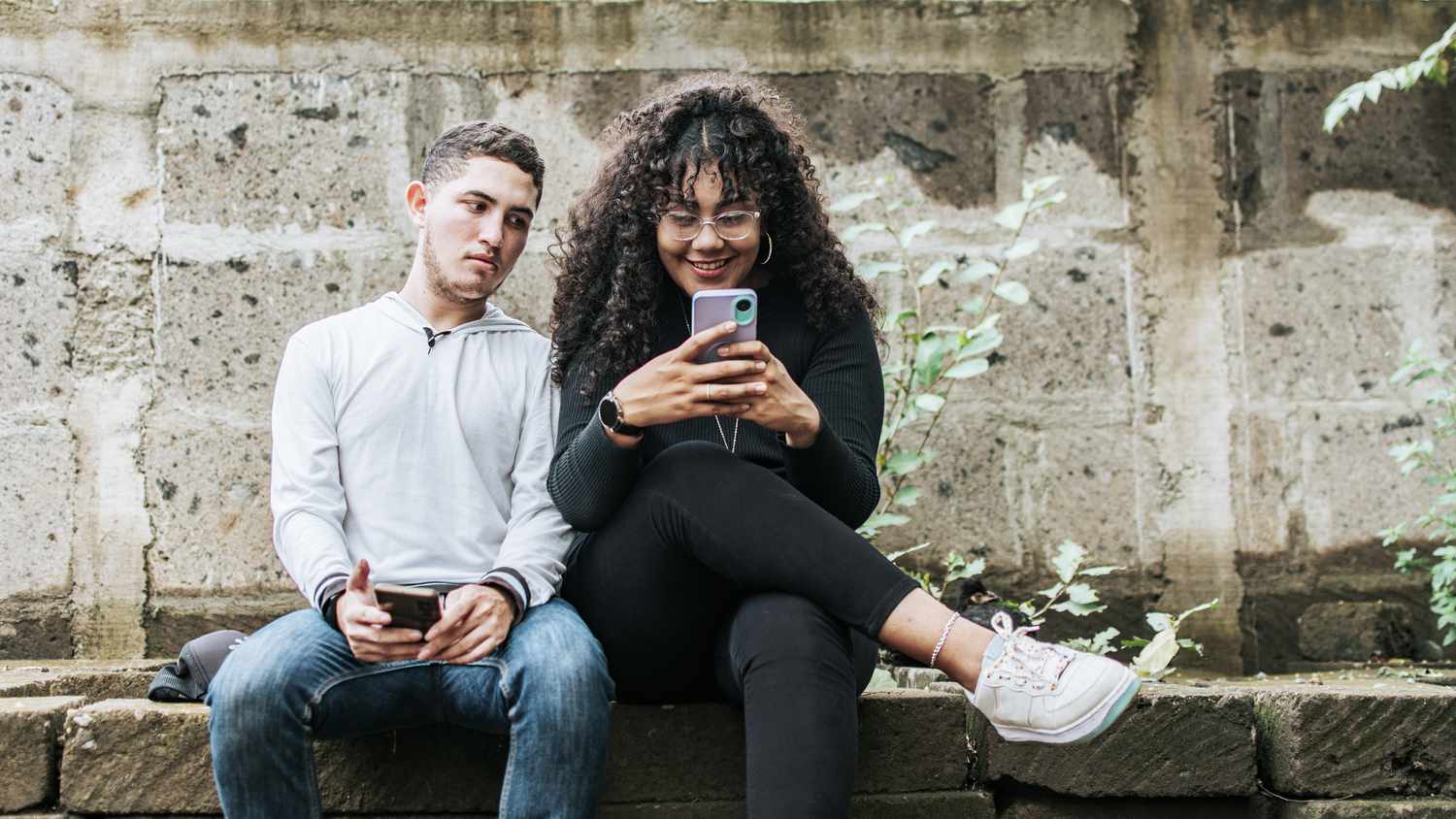 Woman busy with her phone, man is looking irritated