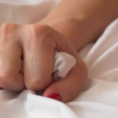 A hand holding the sheets in bed