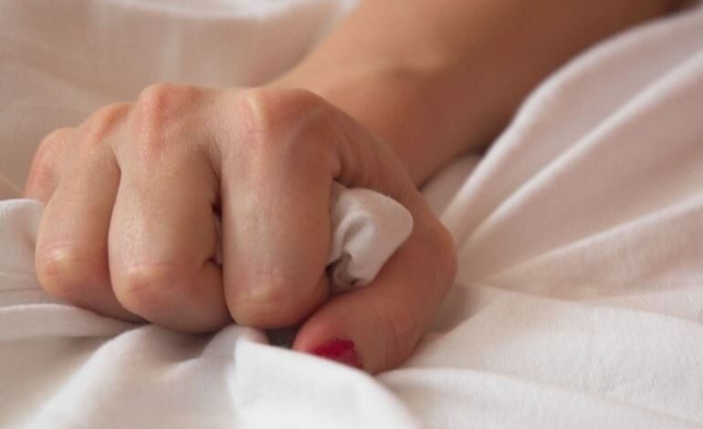 A hand holding the sheets in bed