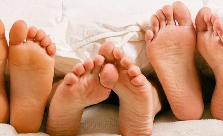 Three pair of feet in bed