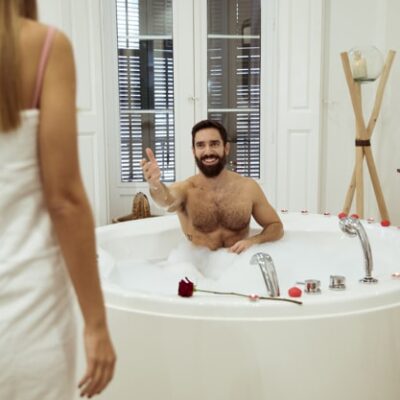Man in bathtubb, woman in bathrobe next to it