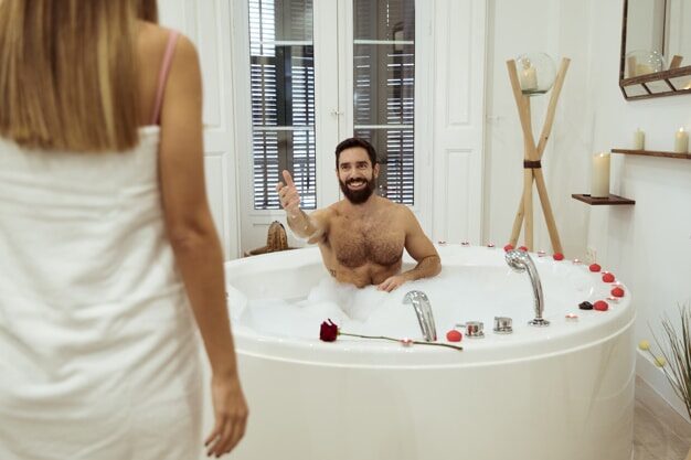 Man in bathtubb, woman in bathrobe next to it