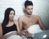 Man en vrouw kijken op een laptop in bed